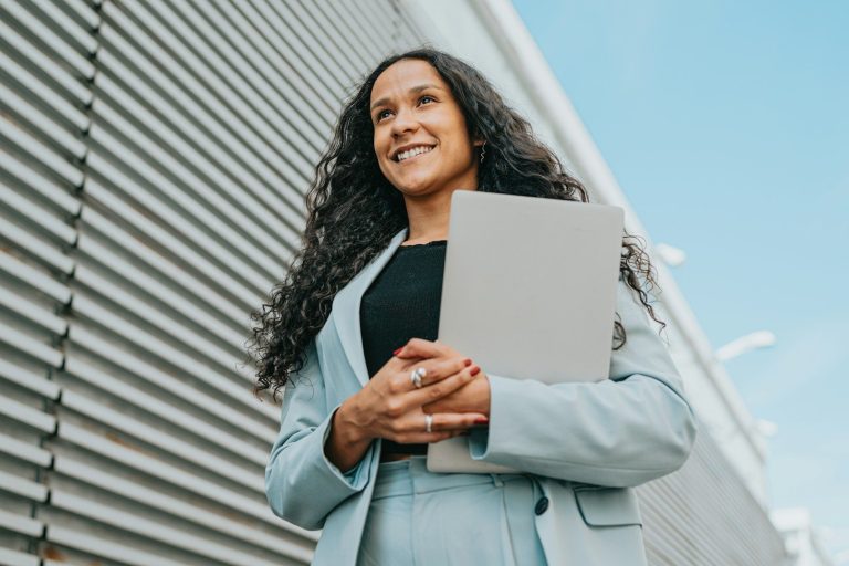 Stärkung der Arbeitgebermarke Eine lächelnde Frau mit einem Notebook neben einem Bürohaus